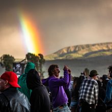 Rainbow in the background with the crowd taking photos in the foreground. 2019 banner flying in the background