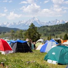 A picture of the camping at Fire in the Mountains 2019 with the Tetons in the background. There are many tents and people having fun